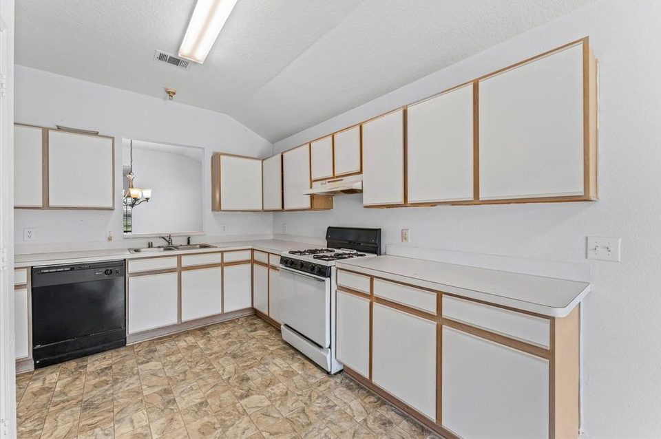 Cocina antes de la remodelación, con gabinetes blancos, bordes de madera y pared cerrada sobre el fregadero.