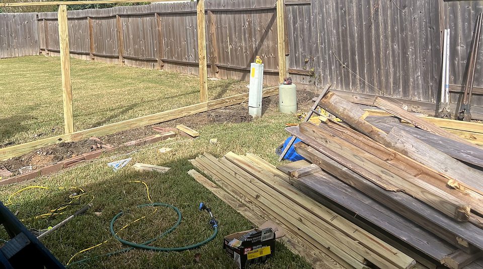New fence posts and rails set in a back yard, with lumber stacked beside them.